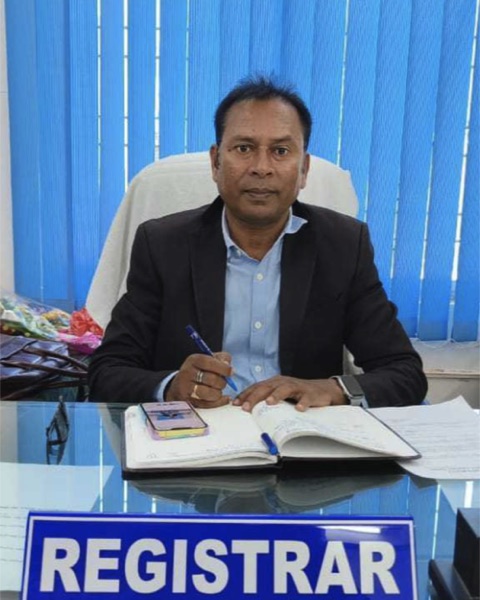 Portrait of Shri Maheshwar Naik, Registrar, at the Registrar's desk.